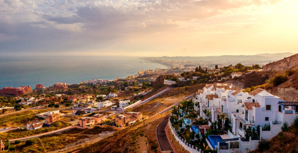 Spanish houses and resorts fill a hillside with the sea in the distance.