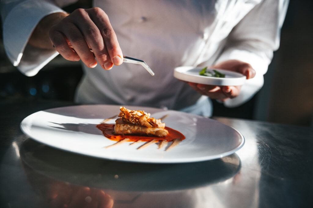 Chef preparing a gilthead bream dish in a luxury restaurant, close up view.