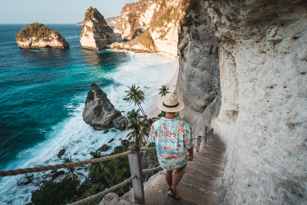 Young Asian traveller walking down to Diamond beach in a morning sunrise in summer season. Nusa Penida island near Bali island, Indonesia, Asia